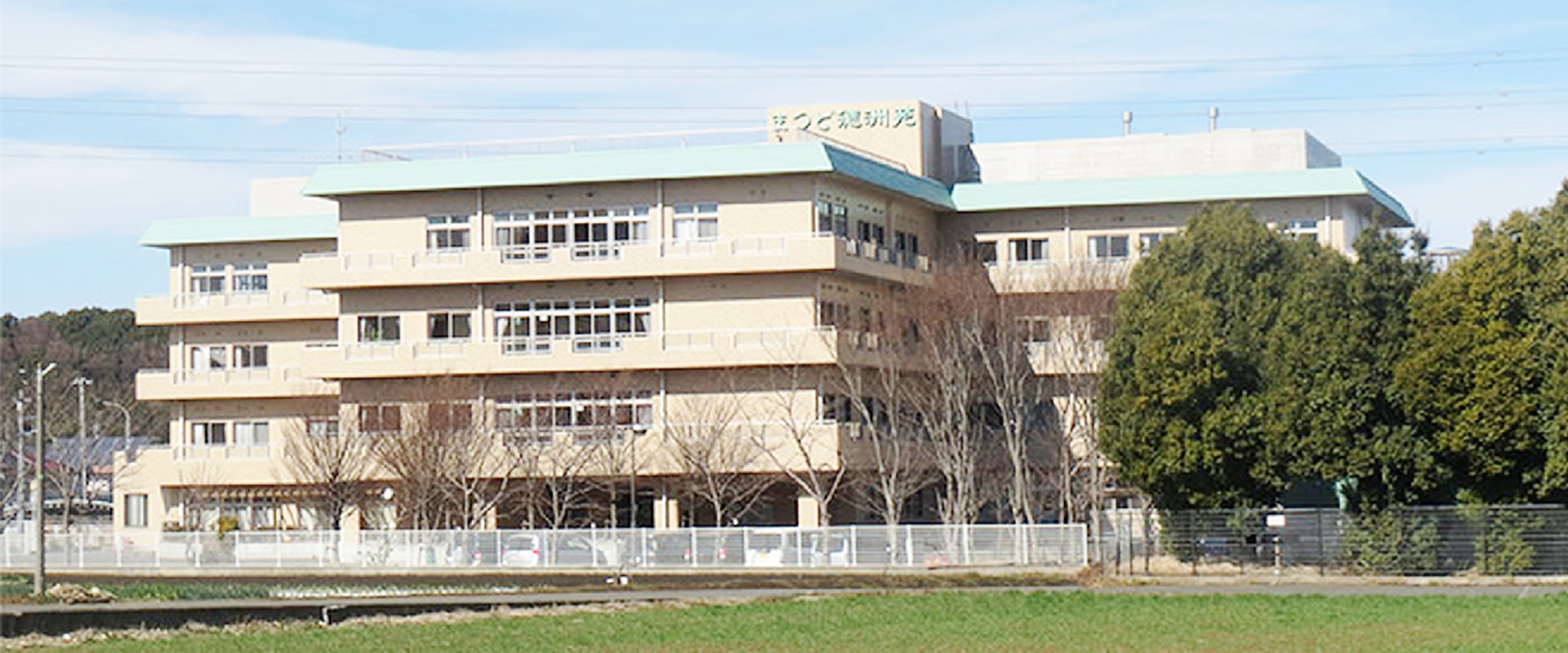 介護施設の全景。複数階の白色建物、緑地帯に面した外観